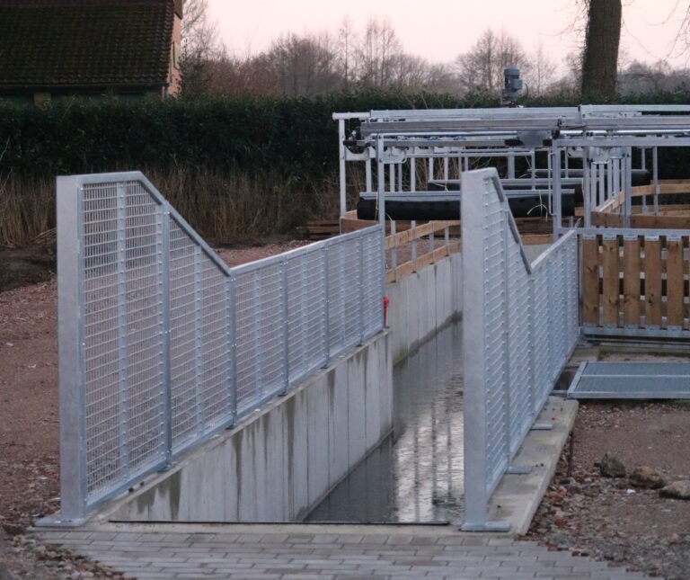 Moderne Wasserführanlage für Pferde mit metallenen Leitgittern und einem Wasserlauf im Außenbereich.